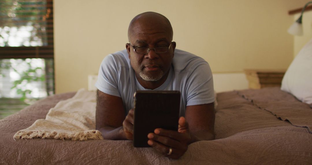 Older Man Reading Tablet While Lying on Bed in Relaxed Setting - Free Images, Stock Photos and Pictures on Pikwizard.com