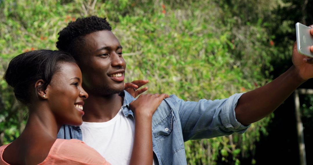 Joyful Couple Taking Outdoor Selfie, Smiling in Lush Greenery