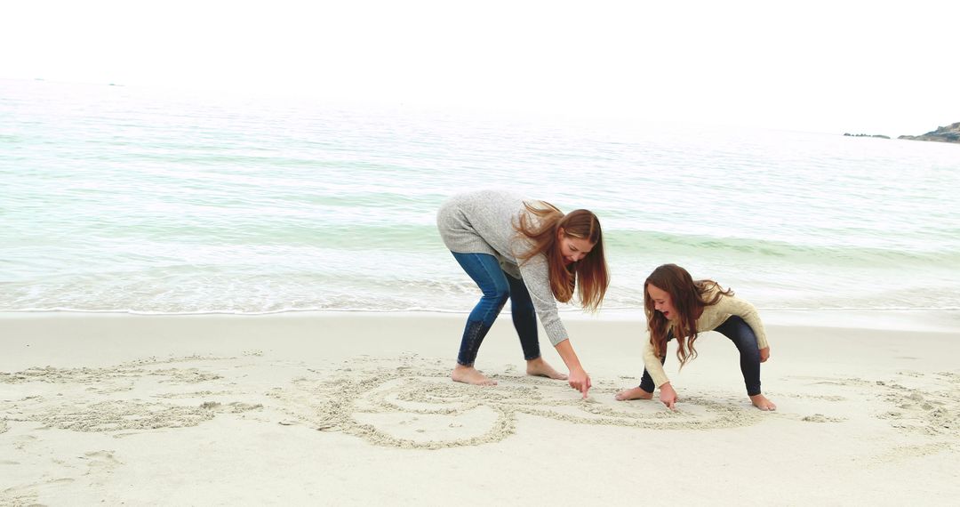 Two Women Writing In The Sand At Seaside - Free Images, Stock Photos and Pictures on Pikwizard.com