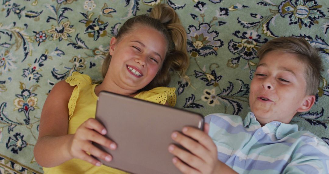 Happy caucasian brother and sister at home, lying on floor using tablet together and smiling - Free Images, Stock Photos and Pictures on Pikwizard.com