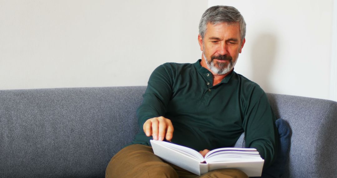 Senior man reading book on sofa with relaxed expression - Free Images, Stock Photos and Pictures on Pikwizard.com