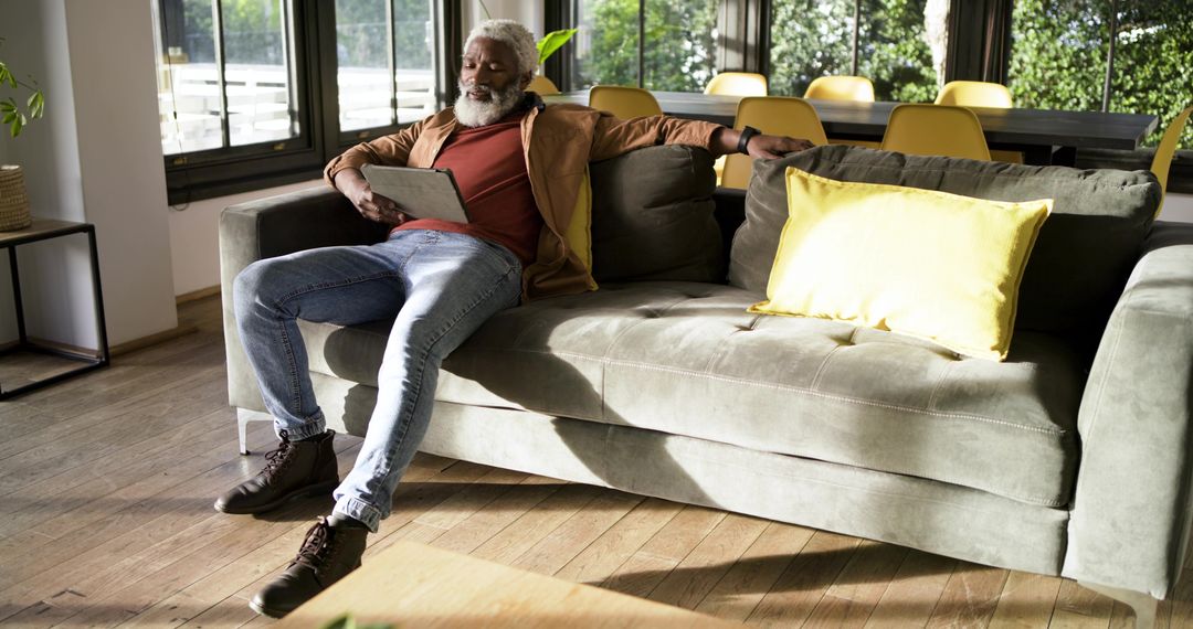 Senior Man Relaxing on Sofa Reading Tablet in Bright Living Room