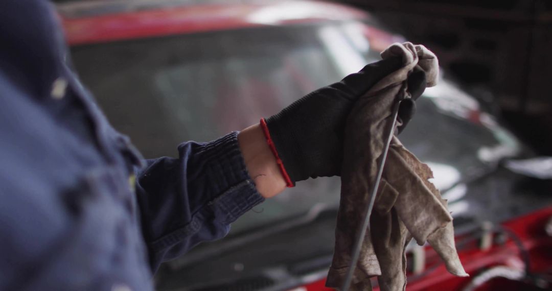 Mechanic inspecting and wiping engine oil dipstick with gloved hand and rag at repair bay