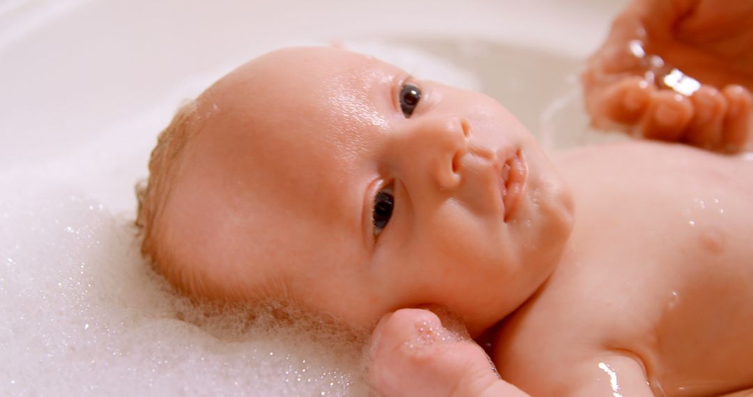 Serene Infant Bath Time with Soothing Bubbles Cradled by Parent - Free Images, Stock Photos and Pictures on Pikwizard.com