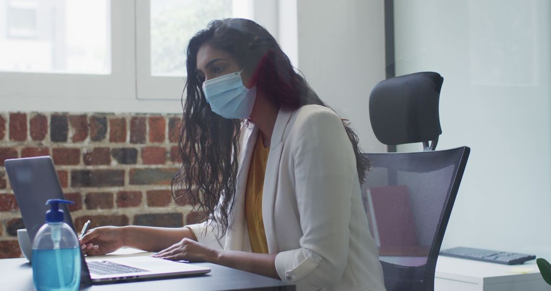 Businesswoman Wearing Face Mask Working on Laptop in Office - Free Images, Stock Photos and Pictures on Pikwizard.com