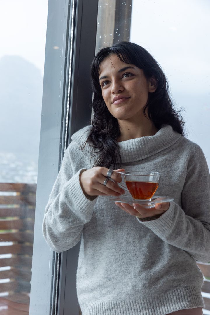 Young Woman Enjoying Tranquil Tea Time Indoors by Large Window