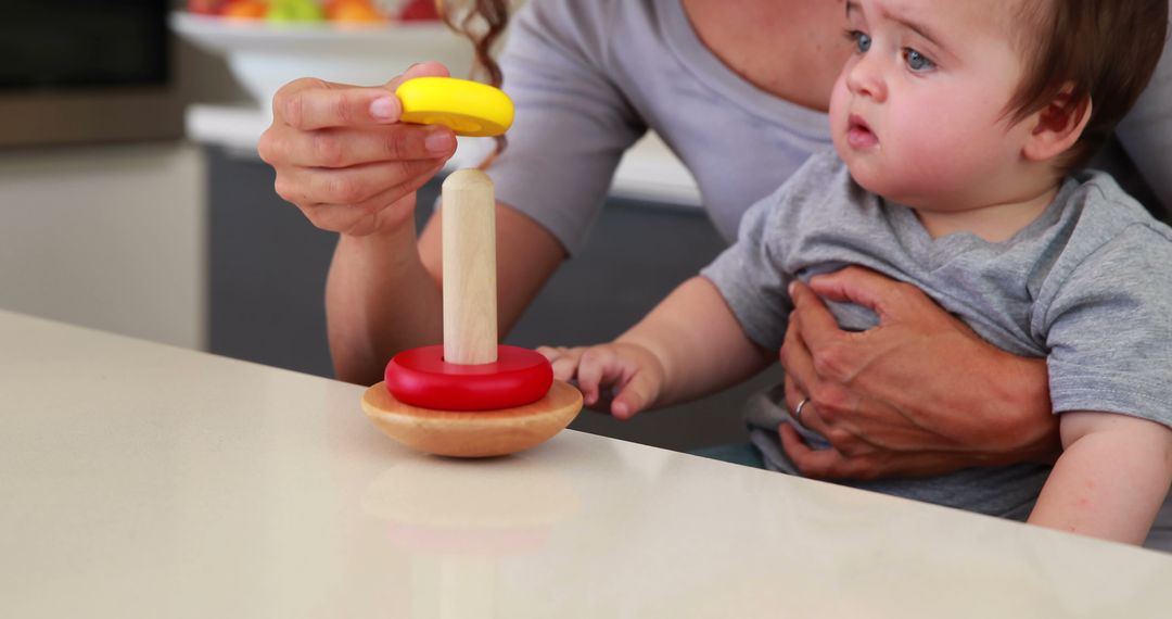 Mother Helping Baby with Stacking Toy at Kitchen Counter - Free Images, Stock Photos and Pictures on Pikwizard.com