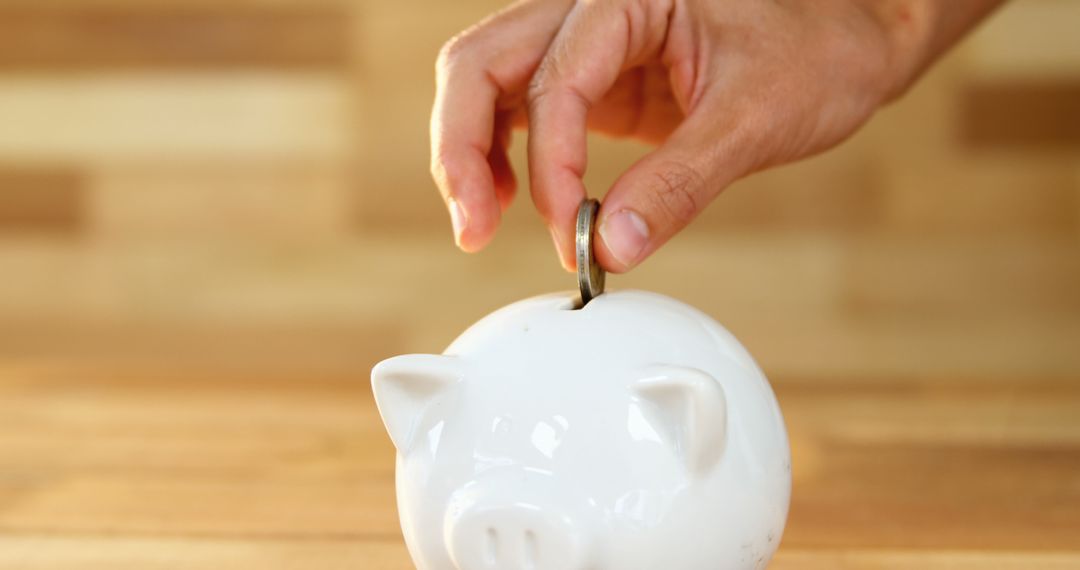 Hand Dropping Coin Into White Piggy Bank on Wooden Surface - Free Images, Stock Photos and Pictures on Pikwizard.com