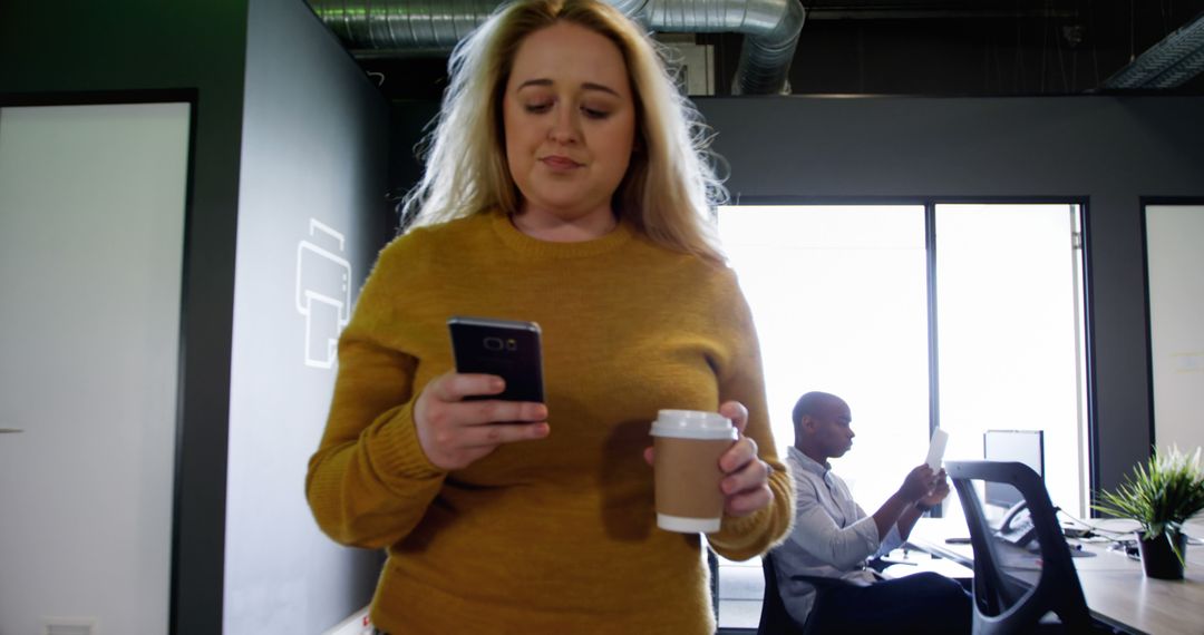 Woman checking smartphone while holding coffee cup in modern office - Free Images, Stock Photos and Pictures on Pikwizard.com