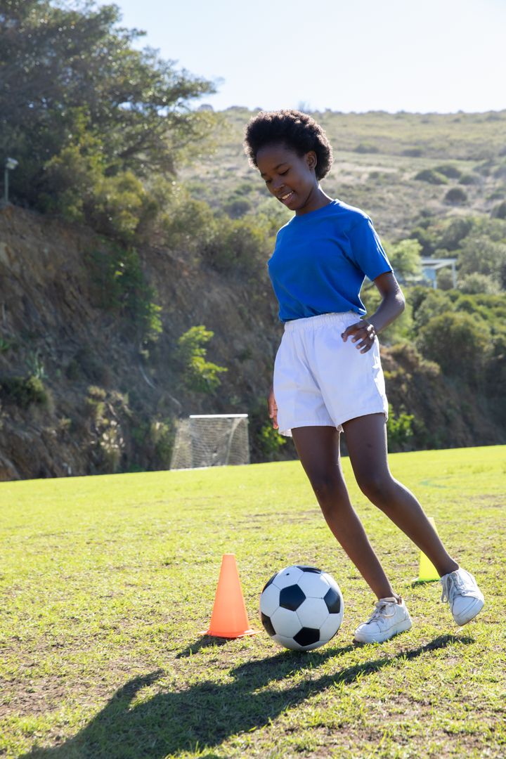 Teen Athlete Practicing Soccer with Ball and Cone on Sunny Field