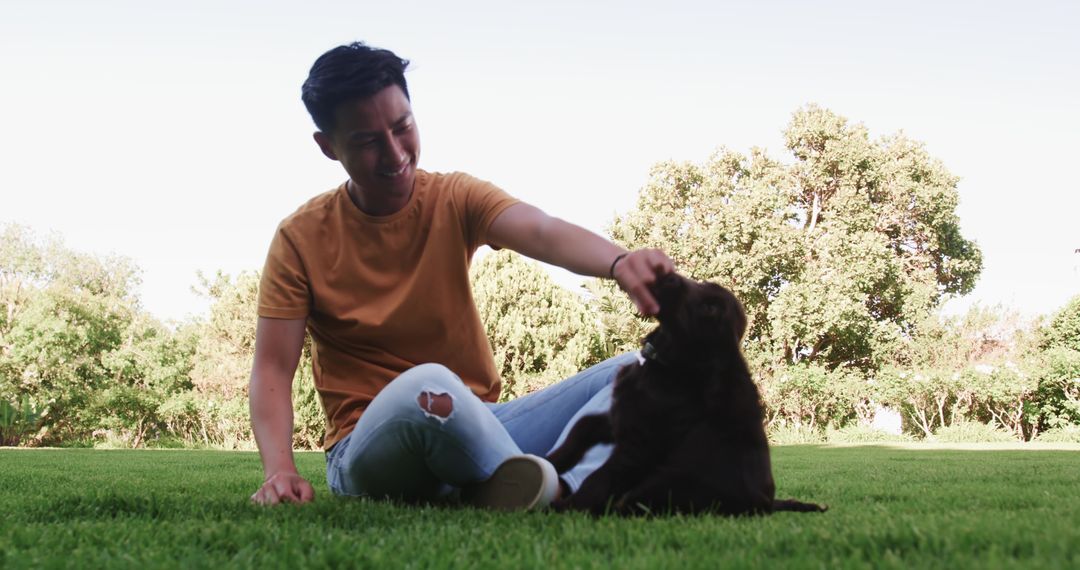 Smiling Man Petting Brown Puppy on Green Lawn