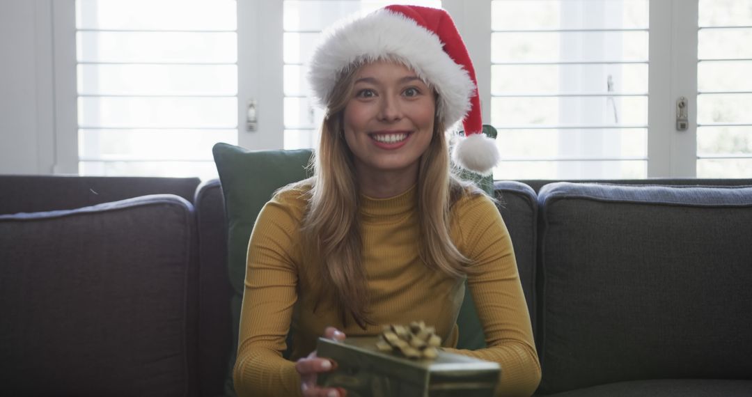 Joyful Woman with Christmas Santa Hat Holding Present at Home - Free Images, Stock Photos and Pictures on Pikwizard.com