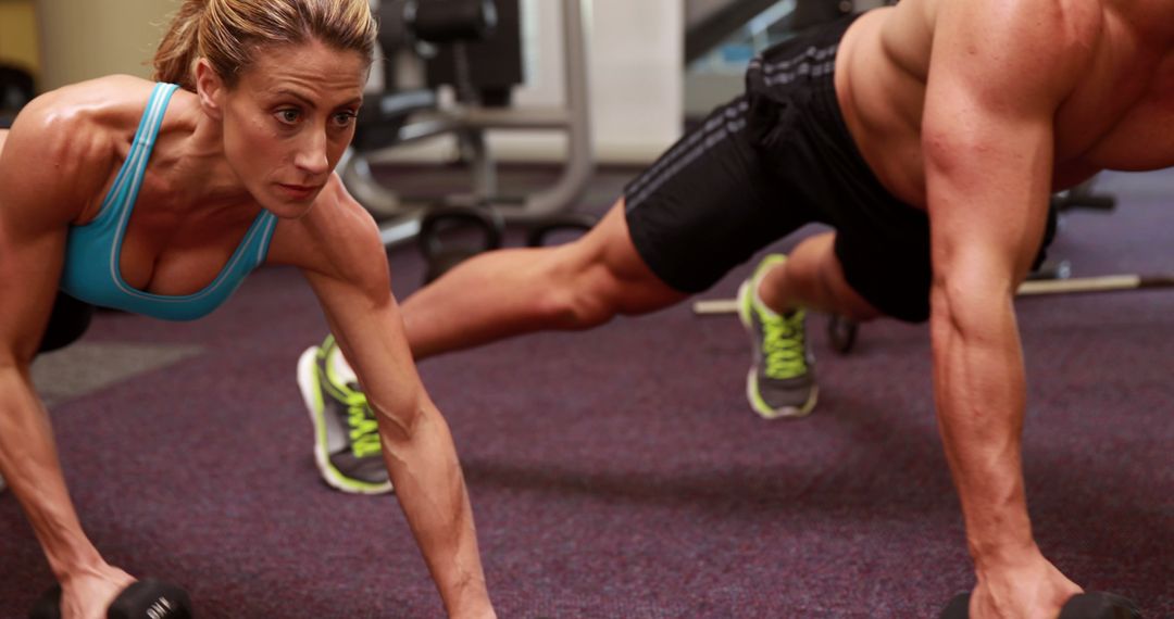 Determined Athletes Performing Plank With Dumbbells in Gym
