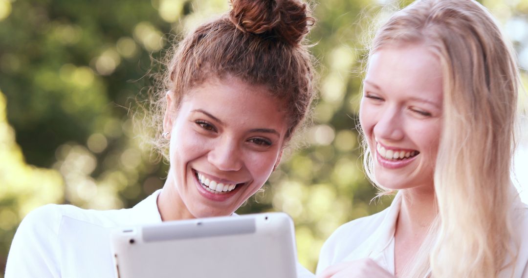 Two young women enthusiastic while using tablet outdoors - Free Images, Stock Photos and Pictures on Pikwizard.com