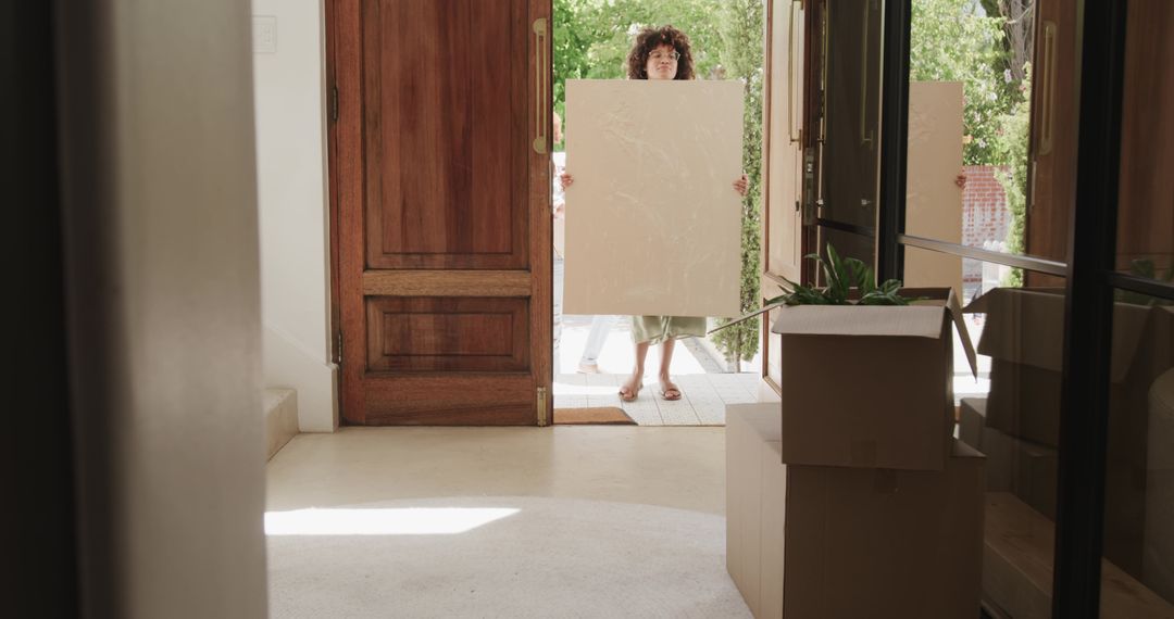 Women Carrying Large Canvas Through Open Front Door During Home Move with Boxes and Sunlit Entryway