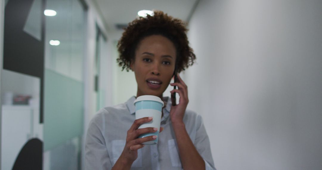 Businesswoman Talking on Phone Holding Coffee Walking Office Hallway - Free Images, Stock Photos and Pictures on Pikwizard.com