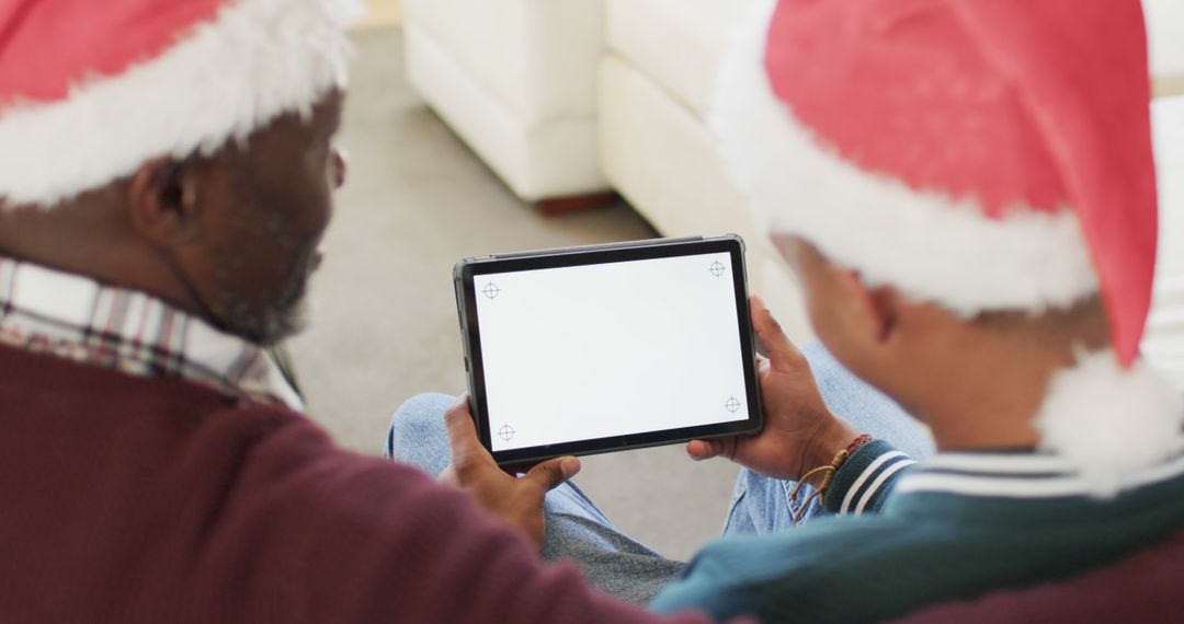 Two People Wearing Santa Hats Using Tablet for Christmas Celebration - Free Images, Stock Photos and Pictures on Pikwizard.com