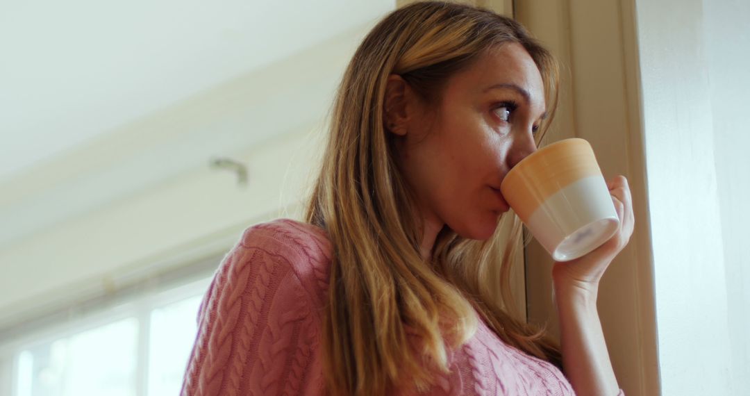 Woman Enjoying Morning Coffee by Window in Pink Sweater - Free Images, Stock Photos and Pictures on Pikwizard.com