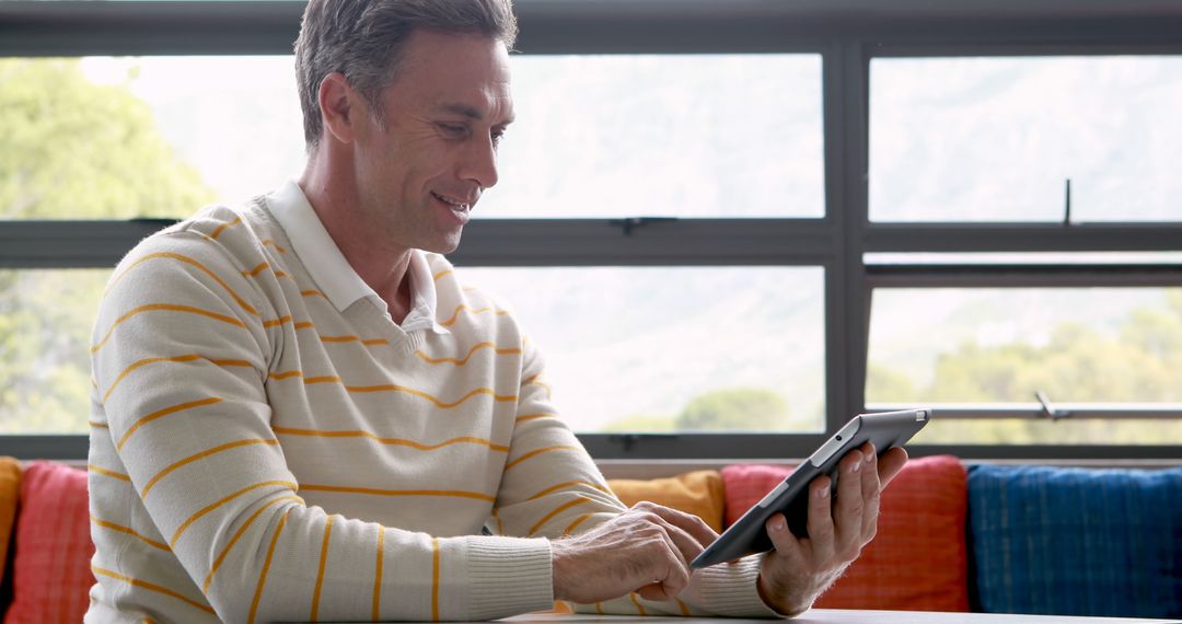 Smiling Man Using Digital Tablet in Bright Living Room - Free Images, Stock Photos and Pictures on Pikwizard.com