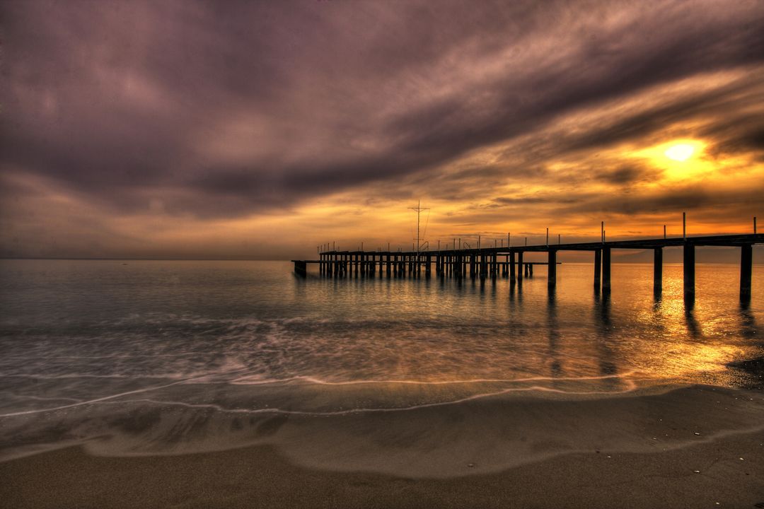 Sunset Over Serene Beach with Pier and Dramatic Sky - Free Images, Stock Photos and Pictures on Pikwizard.com