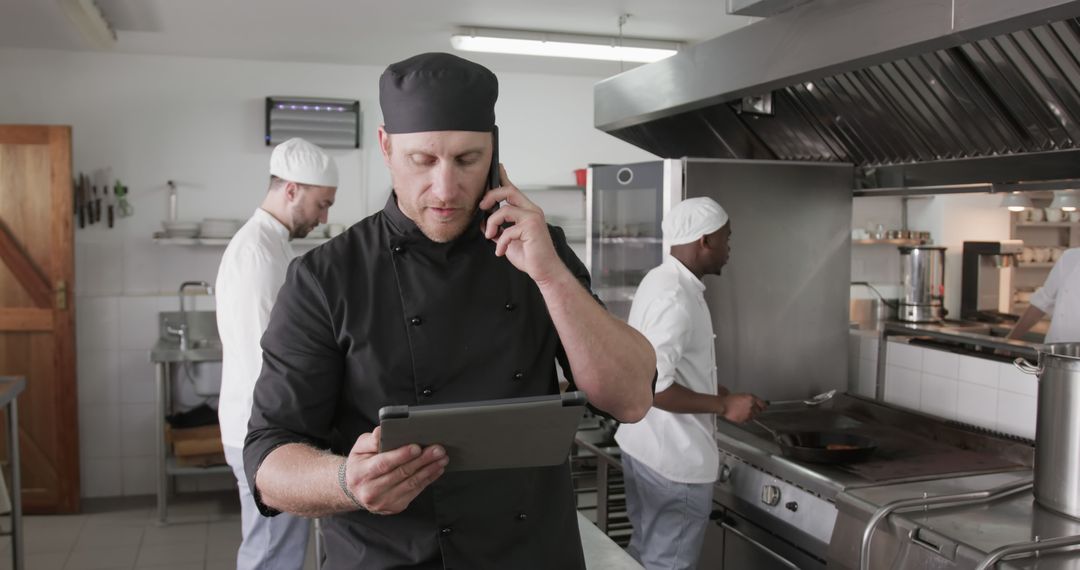 Restaurant Chef Talking on Phone While Using Tablet in Professional Kitchen - Free Images, Stock Photos and Pictures on Pikwizard.com