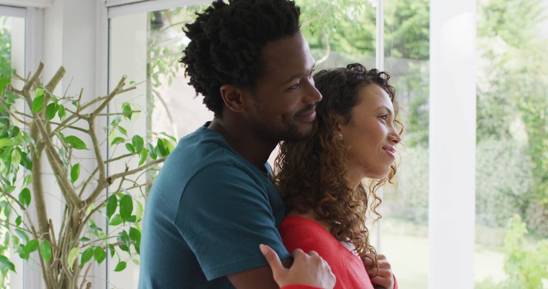 Multiracial Couple Embracing by Window Relaxing at Home Together