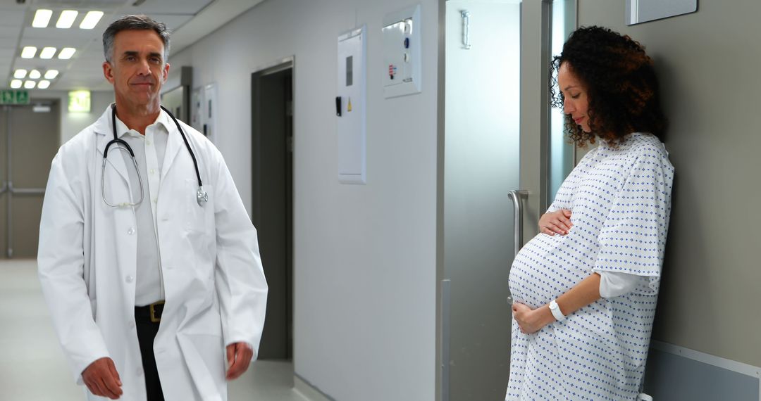 Pregnant Woman Standing in Hospital Corridor with Doctor Walking By - Free Images, Stock Photos and Pictures on Pikwizard.com