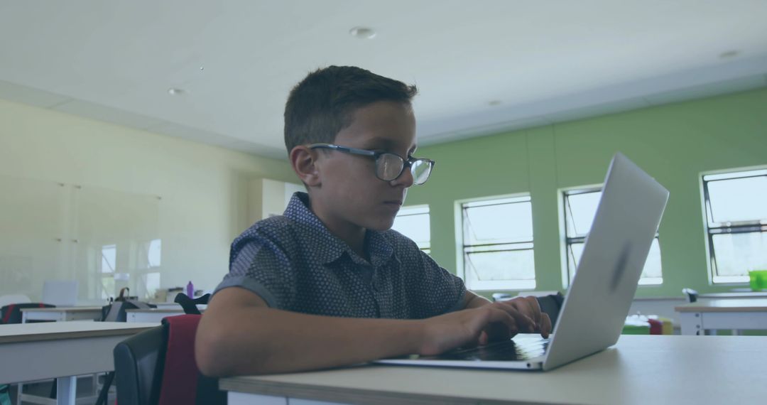 Young student typing on laptop in classroom wearing glasses focusing on digital learning