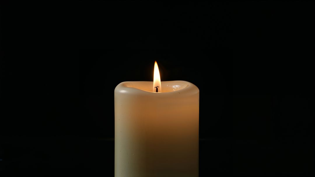 Ivory pillar candle against black background illuminating dark studio for condolences