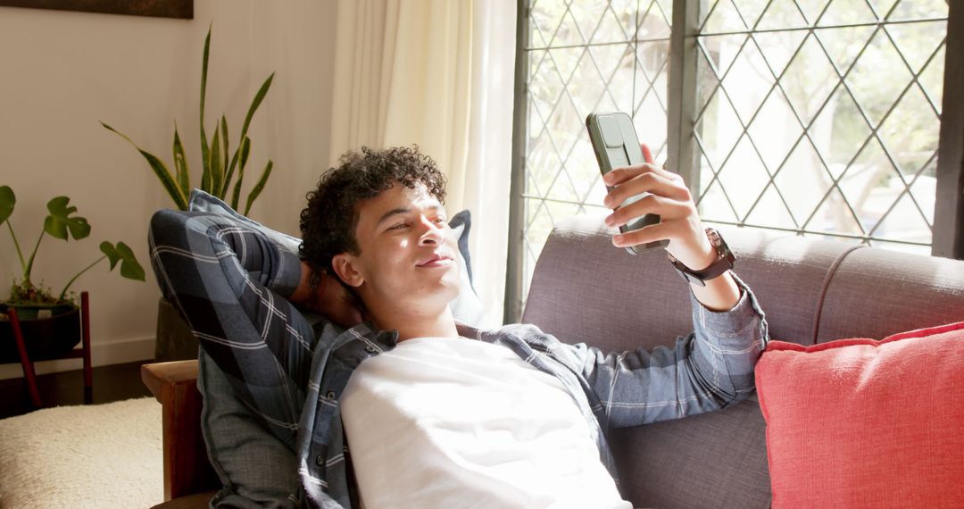 Young Man Relaxing on Sofa Using Smartphone in Sunlit Living Room - Free Images, Stock Photos and Pictures on Pikwizard.com