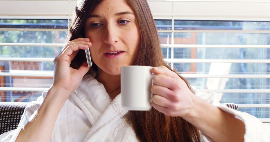 Woman in Bathrobe Drinking Coffee and Talking on Phone Near Window - Free Images, Stock Photos and Pictures on Pikwizard.com