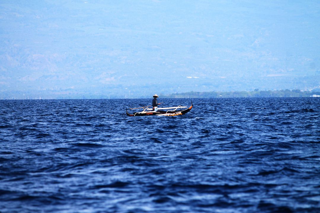 Fisherman alone in traditional fishing boat on vast blue ocean - Free Images, Stock Photos and Pictures on Pikwizard.com