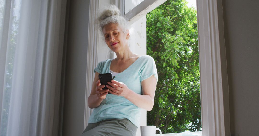 Senior Woman Relaxing by Window Using Smartphone at Home - Free Images, Stock Photos and Pictures on Pikwizard.com