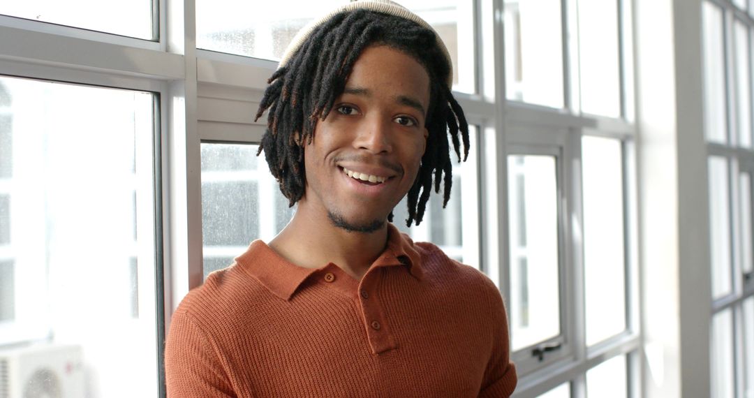 Smiling African American man leaning against windows in loft wearing rust sweater and headband