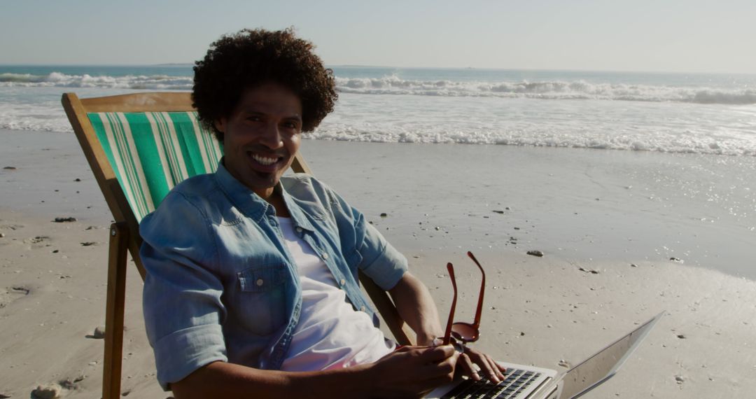 Smiling Man Working on Laptop While Sitting on Beach Chair by Ocean - Free Images, Stock Photos and Pictures on Pikwizard.com