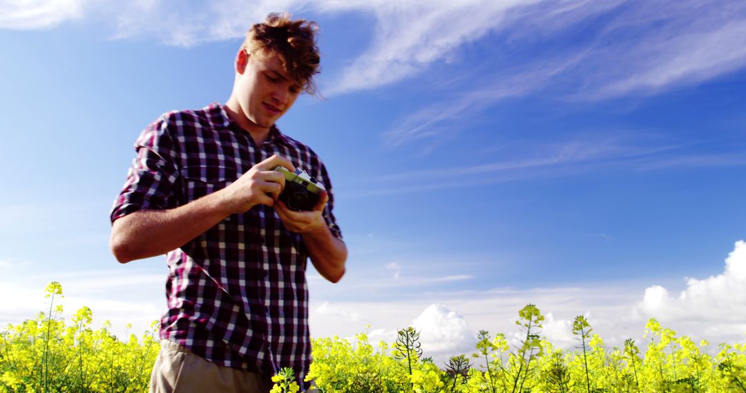 Young Man in Plaid Shirt Adjusting Camera in Bright Yellow Field - Free Images, Stock Photos and Pictures on Pikwizard.com