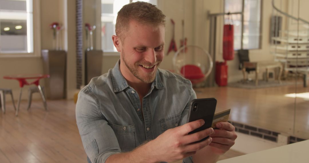 Smiling Man Making Online Purchase on Smartphone in Modern Apartment - Free Images, Stock Photos and Pictures on Pikwizard.com