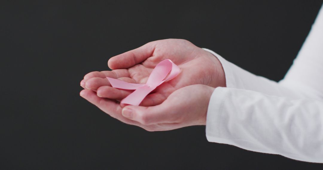 Hands Holding Pink Breast Cancer Awareness Ribbon on Black Background - Free Images, Stock Photos and Pictures on Pikwizard.com