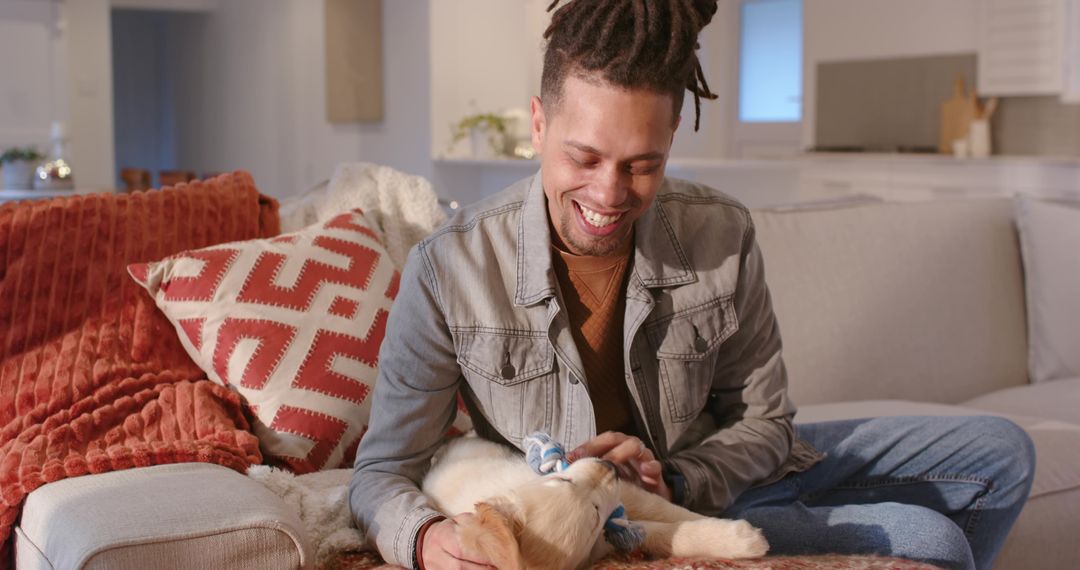 African American man smiling while petting golden retriever puppy on cozy modern sofa
