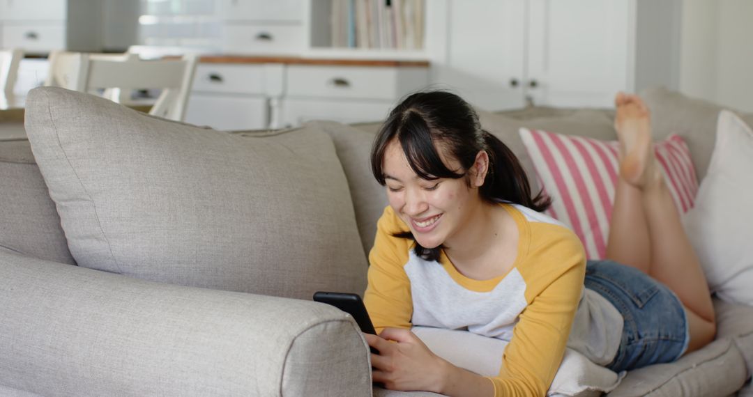 Asian Woman Relaxing on Couch Using Smartphone at Home