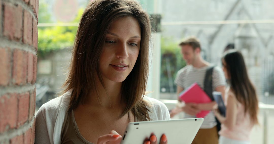 Young Woman Using Tablet Outdoors with Friends in Background - Free Images, Stock Photos and Pictures on Pikwizard.com