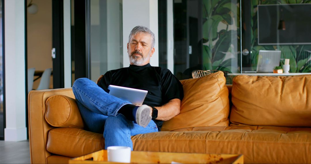 Older Man Relaxing on Couch Using Tablet in Modern Living Room - Free Images, Stock Photos and Pictures on Pikwizard.com