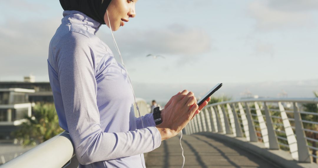 Muslim Woman in Sportswear Taking a Break on Bridge with Smartphone - Free Images, Stock Photos and Pictures on Pikwizard.com