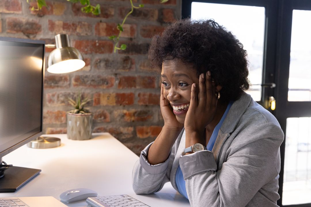 Joyful Professional Sitting at Desk Smiling at Computer Monitor