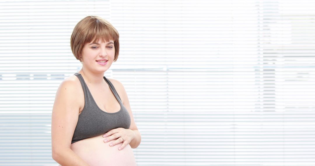 Pregnant Woman Holding Belly in Sports Bra Smiling - Free Images, Stock Photos and Pictures on Pikwizard.com