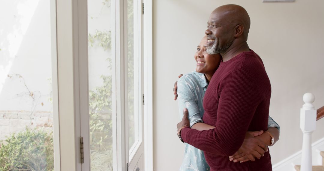 Senior Couple Embracing and Looking Out Window of Modern Home
