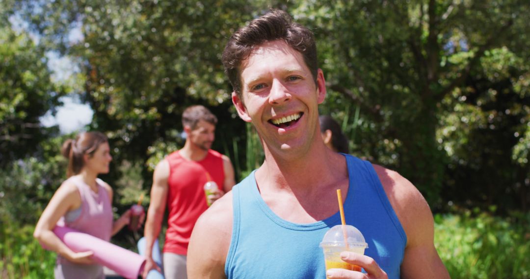 Smiling Man Holding Smoothie in Park with Friends After Yoga