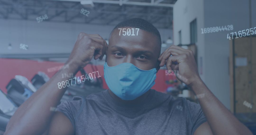 Man Putting on Face Mask in Gym with Floating Numbers