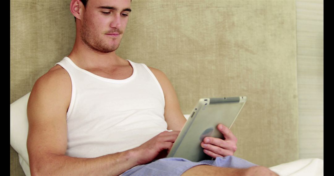 Young Man Relaxing on Bed Using Tablet in Casual Attire - Free Images, Stock Photos and Pictures on Pikwizard.com