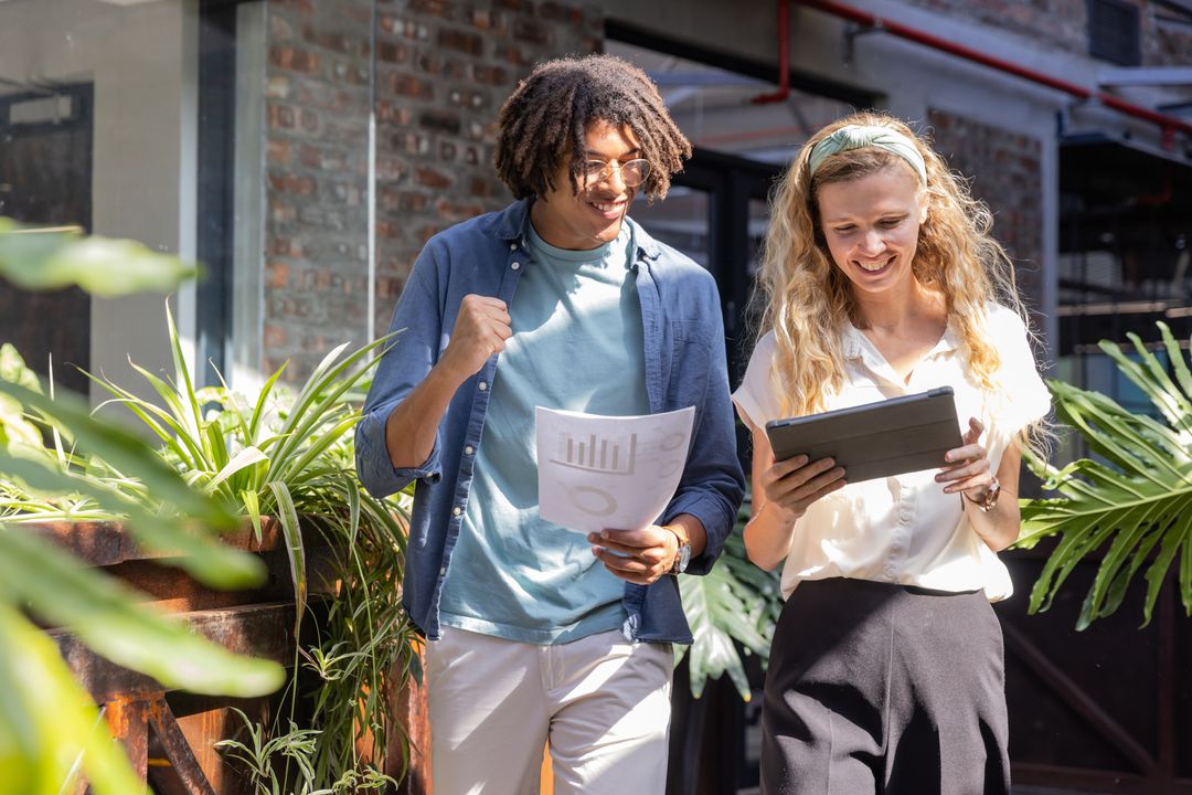 Diverse Colleagues Sharing Ideas in Office Courtyard with Tablet and Charts